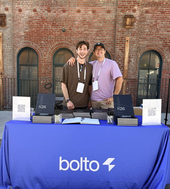 Two Bolto teammates behind a Bolto-branded table at an outdoor event.